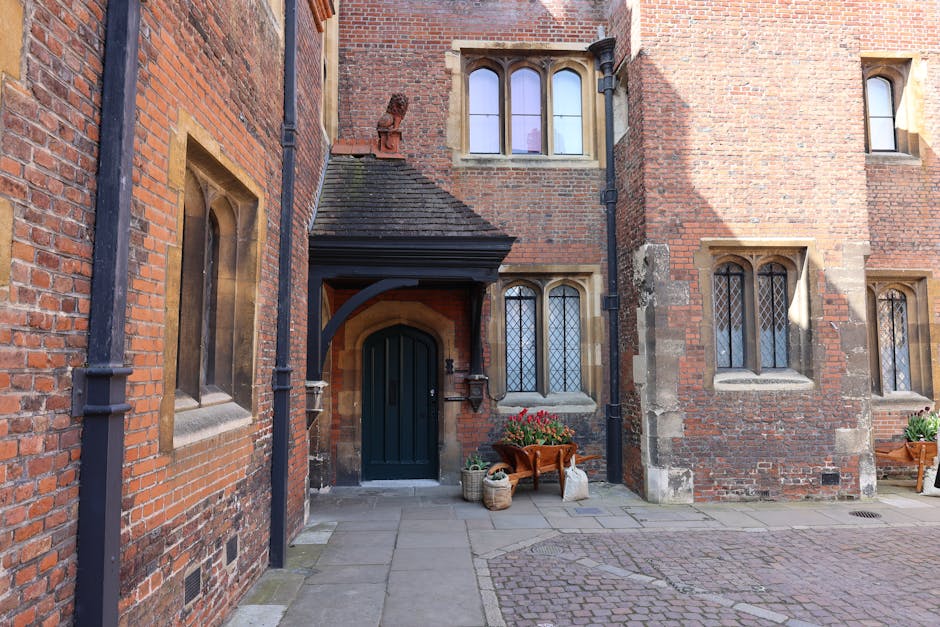 Exterior view of Lambeth Palace, a historic brick building with crenellated battlements and tall, arched white-framed windows, set against a vivid blue sky with scattered white clouds. The brickwork showcases a consistent red hue with some weathered textures, highlighting the Gothic architectural style. The facade includes multiple windows with decorative arches, and a small stone balcony with a lantern hanging at the entrance. The image captures the grandeur and classic detailing of the palace exterior, reflecting its historic significance and well-maintained appearance, typical of expert surface cleaning and preservation efforts by Lambeth Carpet Cleaning.